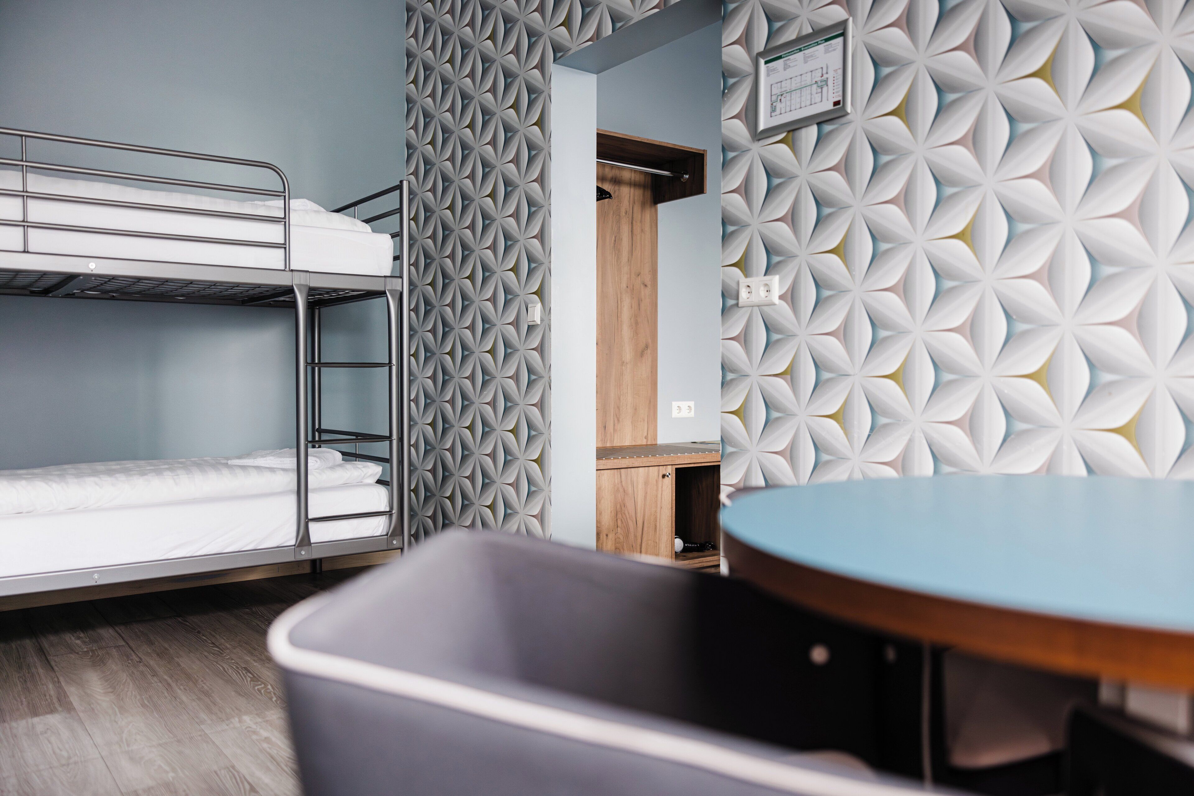 A bunk bed room with a geometric patterned wall, a small table, and a wooden cabinet.