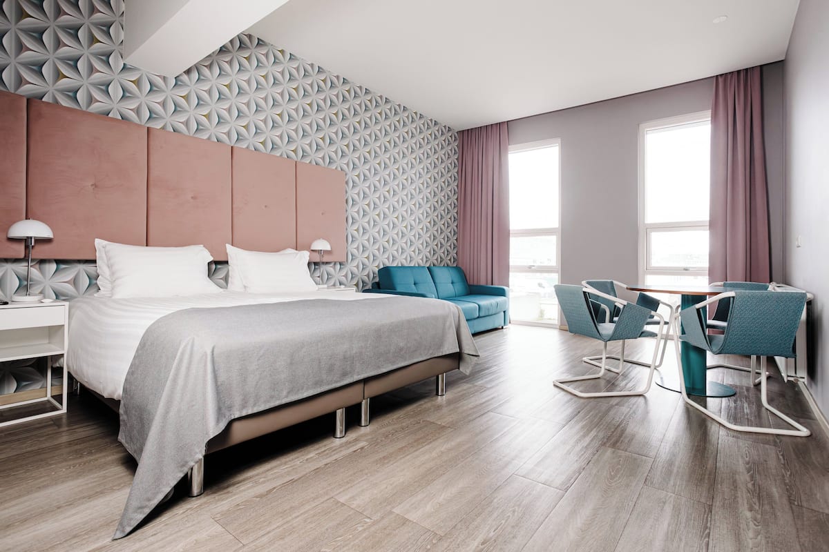 Una habitación de hotel moderna con una cama grande, un escritorio con dos sillas, un sofá azul y una pared con estampado.