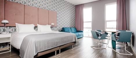 Una habitación de hotel moderna con una cama grande, un escritorio con dos sillas, un sofá azul y una pared con estampado.
