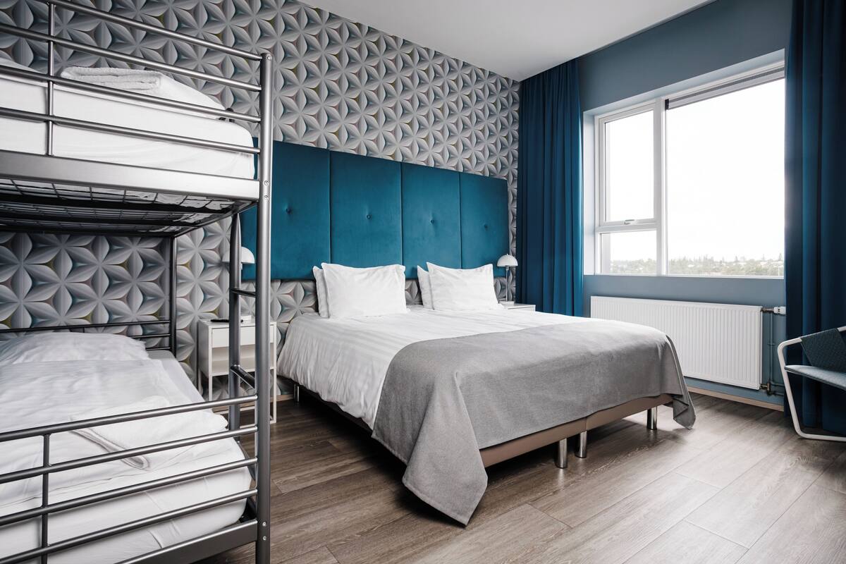 Habitación con literas, pared con estampado geométrico, ventana grande con cortinas y vista a la ciudad.
