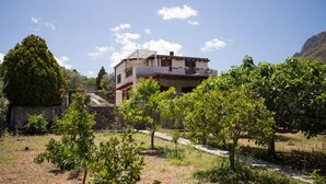 A two-story building with a balcony, surrounded by a vineyard and a stone wall.