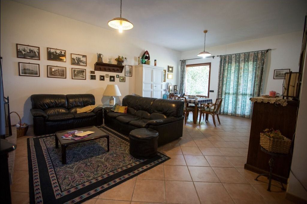 Un salon comprenant un canapé, une table basse et un tapis. Les murs sont ornés de tableaux encadrés, et un coin repas est aménagé avec des chaises et une table.