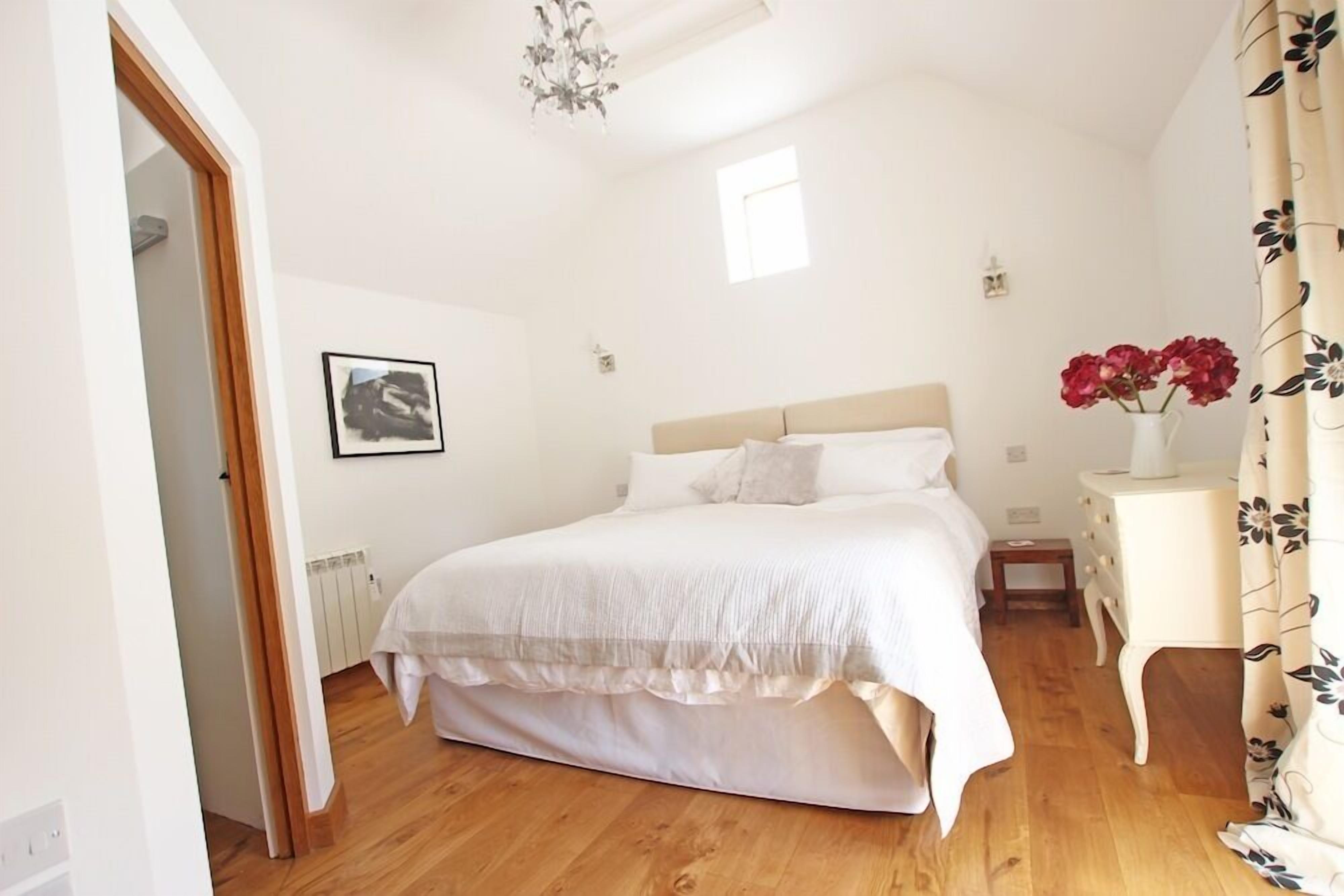 A bedroom with a large bed, a nightstand, a small table, a radiator, a picture on the wall, and a window.