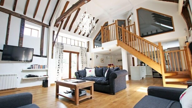 A spacious living room with a wooden staircase, a flat-screen TV, and a cozy seating area.