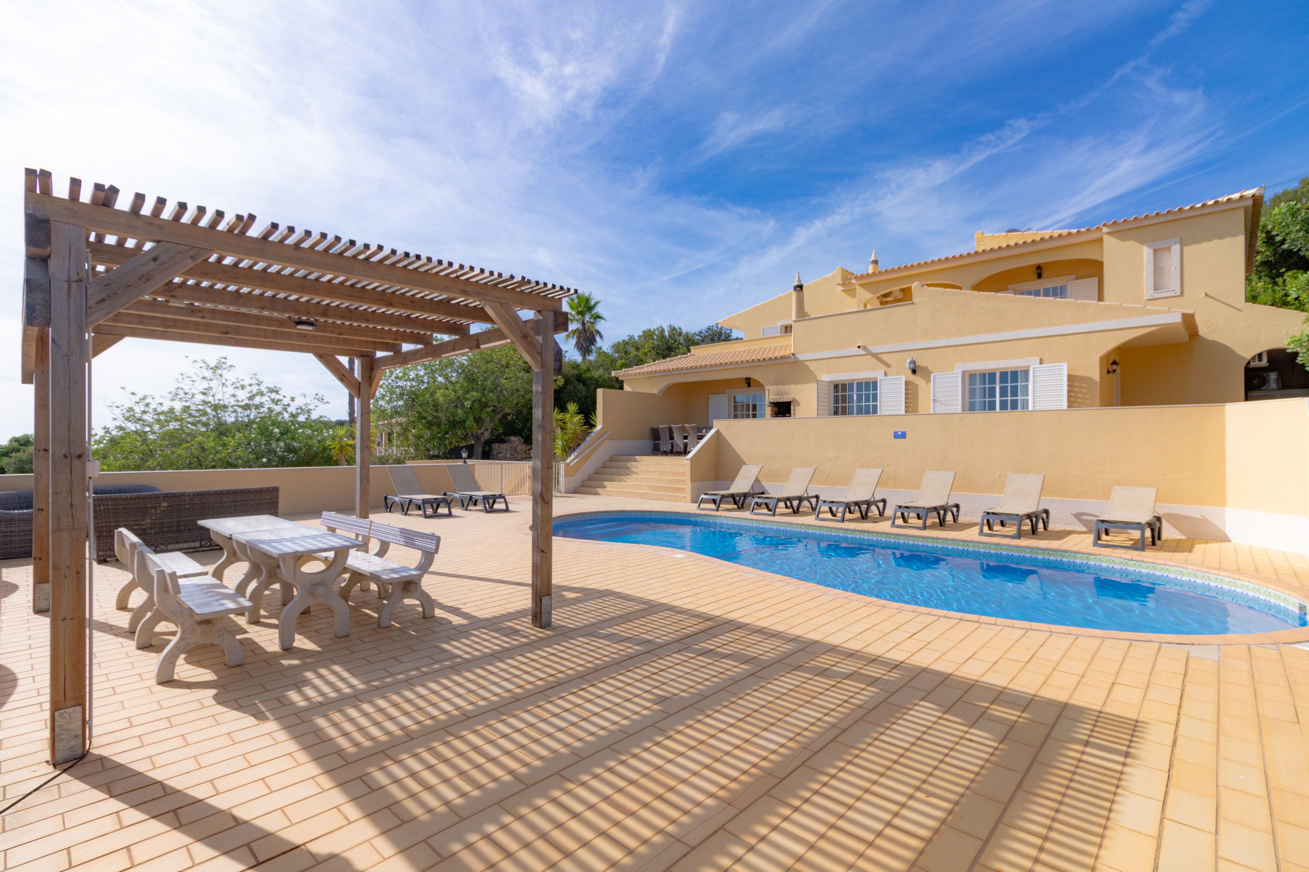 A poolside area with a pergola, lounge chairs, and a swimming pool.