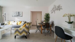 Een moderne woonkamer met een bank, fauteuils, een eettafel met stoelen en een potplant.