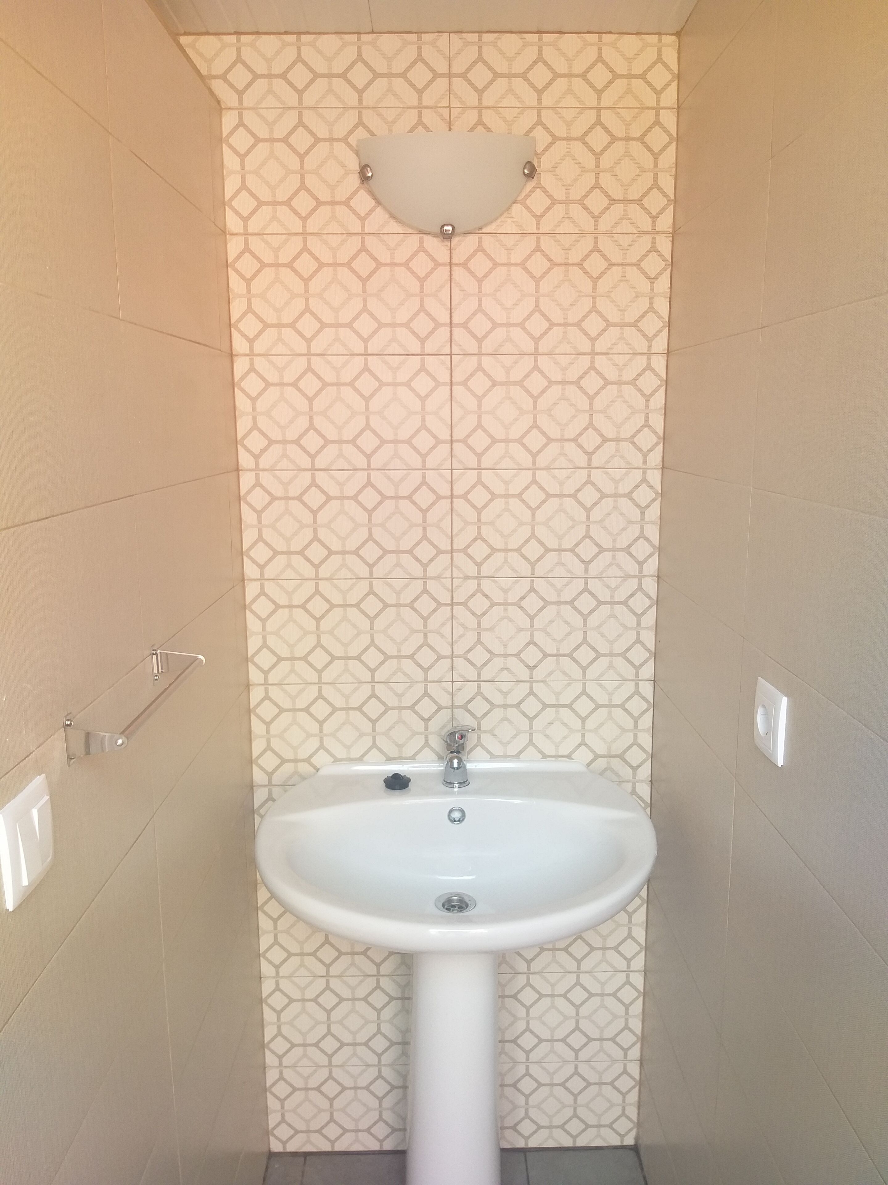 Une salle de bain avec un lavabo sur colonne blanc, un porte-serviettes fixé au mur et un pare-feu en carreaux à motifs.
