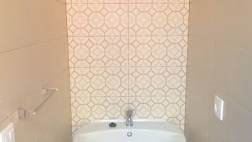 Une salle de bain avec un lavabo sur colonne blanc, un porte-serviettes fixé au mur et un pare-feu en carreaux à motifs.