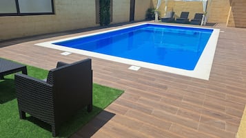 A rectangular swimming pool with a wooden deck and artificial grass.
