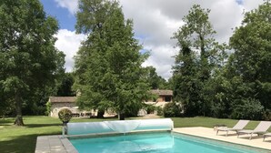 Une piscine à l’eau d’un bleu limpide, entourée d’une pelouse et d’arbres.