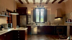 A kitchen with wooden cabinets, a built-in oven, a microwave, and a window with a view of trees. - Costabravapartment Can Marc with private pool and tennis court (Massanes (Girona))