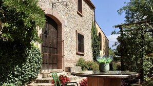 A stone building with a wooden door, a metal gate, and a small table with a potted plant. - Costabravapartment Can Marc with private pool and tennis court (Massanes (Girona))