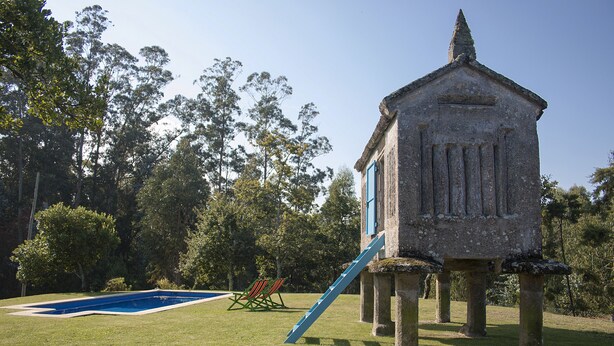 A stone structure with a blue door and a slide, surrounded by a grassy area and trees.