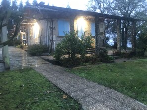 Un chemin de pierres mène à un bâtiment rustique doté d’un porche abrité et d’un petit jardin.