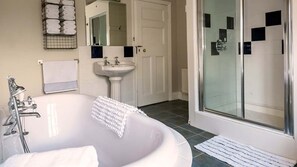 Un baño con bañera independiente, lavamanos, espejo y zona de ducha.