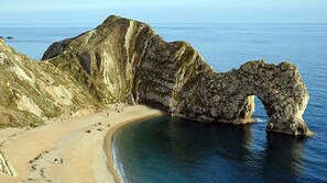 Un paisaje costero con una formación rocosa prominente en forma de arco sobre la playa.