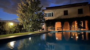 Una piscina con reflejos, rodeada por un jardín y un edificio con balcón.