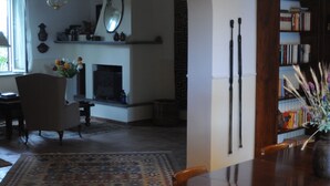 Un comedor con una mesa redonda, sillas, una lámpara de araña, chimenea y una estantería.