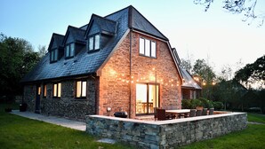 A stone house with a sloped roof, a patio with outdoor furniture, and a stone wall surrounding the property. - Great House nr Polzeath on golf course ideal for families (St Minver, Near Wadebridge)