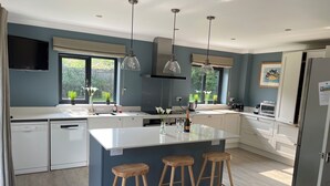 A modern kitchen with a central island, wooden stools, and a built-in dishwasher. - Great House nr Polzeath on golf course ideal for families (St Minver, Near Wadebridge)