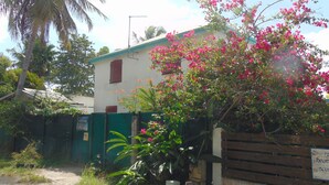 A building with a green fence, a wooden gate, and pink flowering trees. - Caribgites, the Butterfly studio (Sainte-Anne)