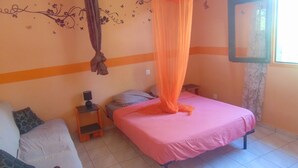 A bedroom with a bed, a nightstand, a chair, and a window with curtains. - Caribgites, the Butterfly studio (Sainte-Anne)