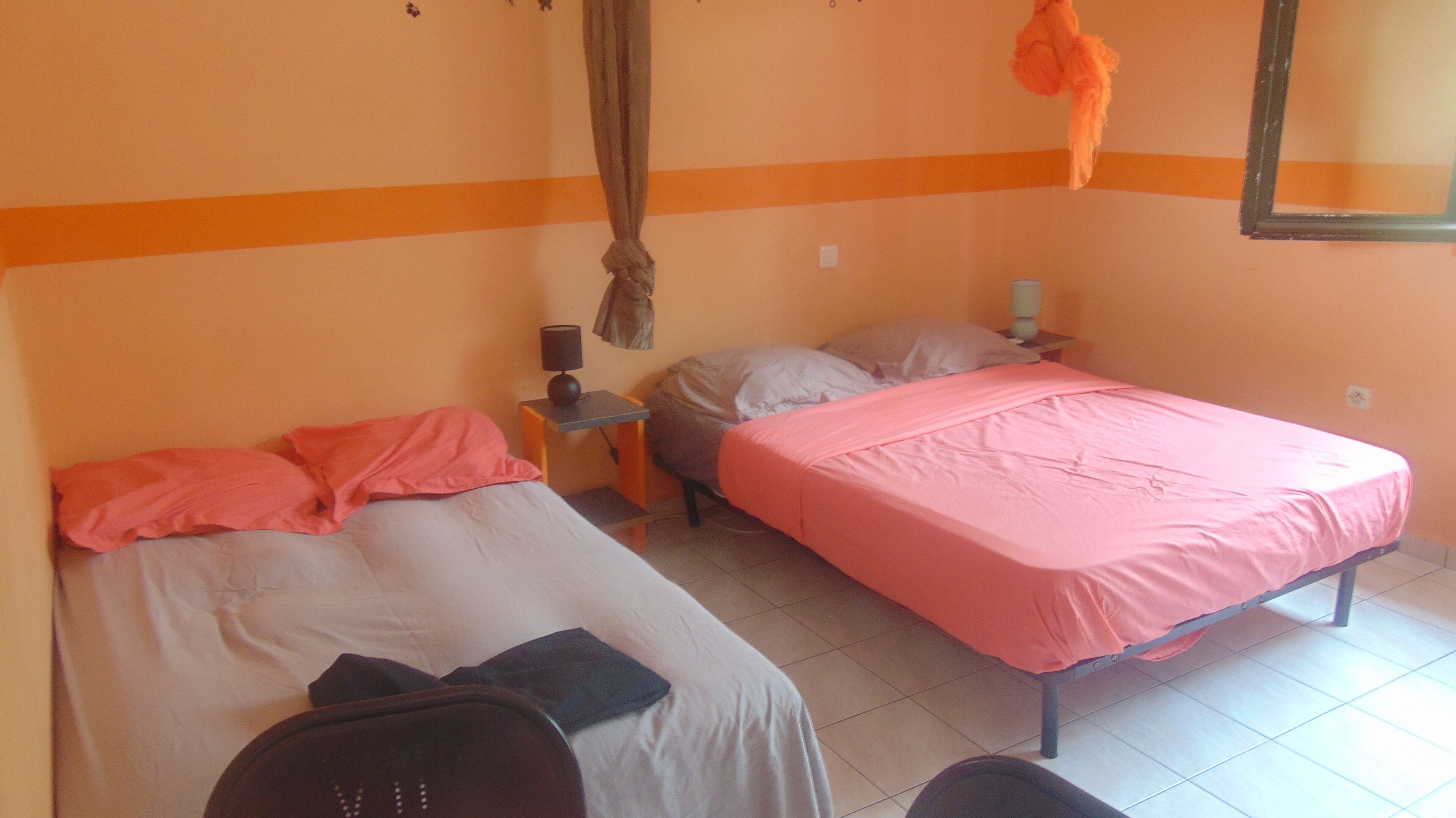 A room with two beds, a small table, a chair, and a hanging curtain.