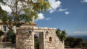 A stone structure with a small arched entrance, surrounded by trees and a view of the sea.