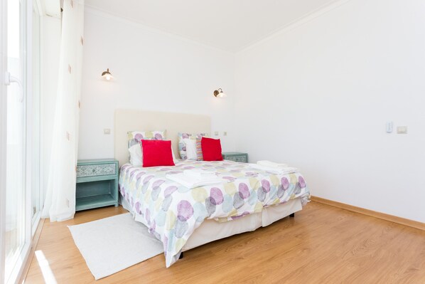 A bedroom with a bed, pillows, bedside tables, and a window.