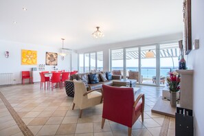 A spacious living area with a view of the sea, a dining area with red chairs, and a kitchen with a white countertop. - CoolHouses Algarve Luz | Casa da Pipa (Luz)