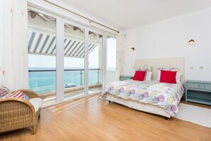 A bedroom with a large bed, a chair, and a view of the sea through a sliding glass door. - CoolHouses Algarve Luz | Casa da Pipa (Luz)