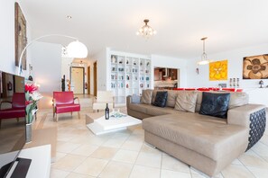 A modern living room with a beige sofa, a red chair, a white coffee table, and a bookshelf.