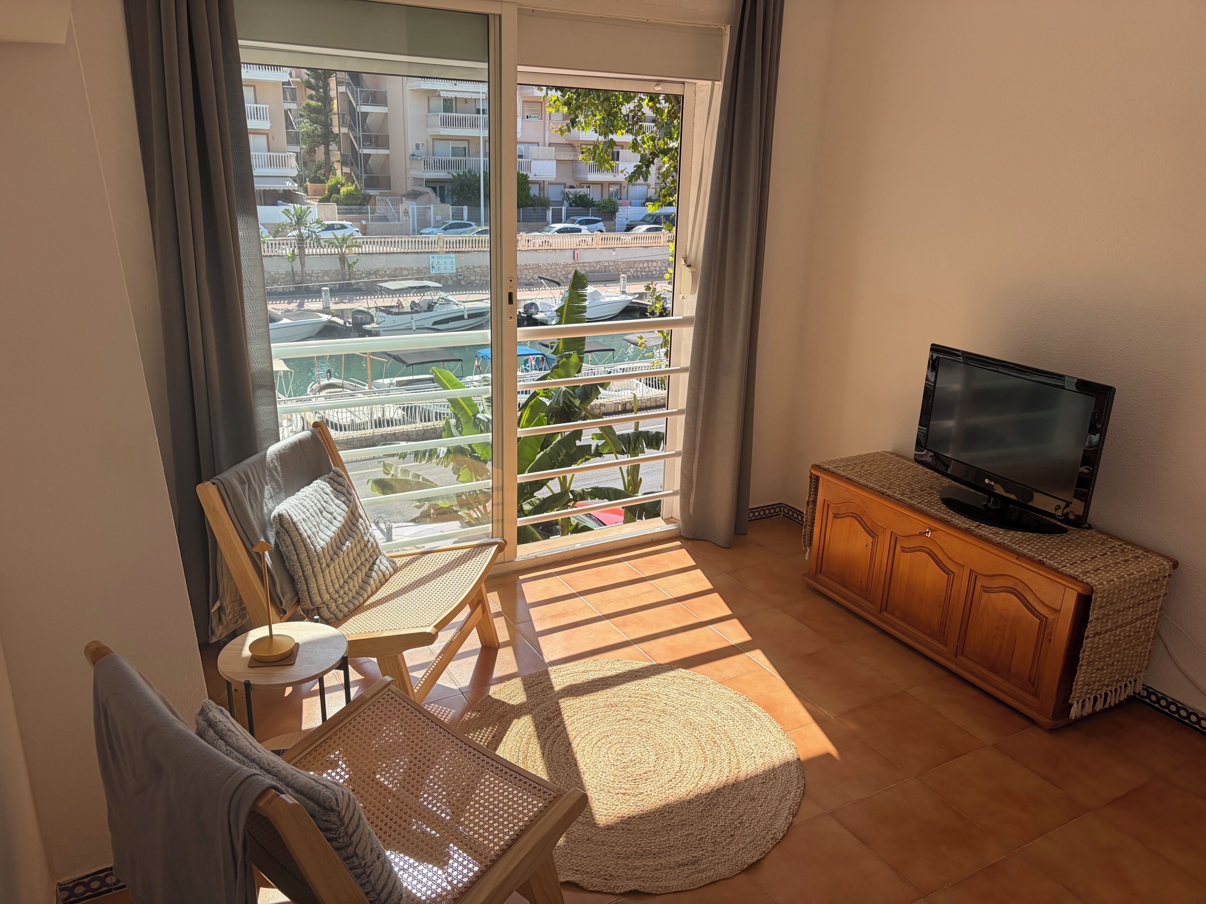 Ein Balkon mit Blick auf eine Marina und Gebäude, ein Fernseher auf einem Schrank sowie eine Sitzecke mit Tisch und Stühlen.