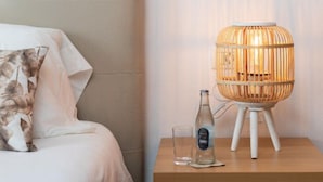 Ein ordentlich bezogenes Bett mit Kissen, ein Nachttisch mit Flasche und Glas sowie eine ungewöhnliche, kugelförmige Lampe.