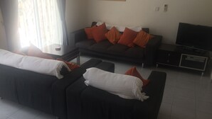Una sala de estar moderna con un sofá oscuro, un televisor de pantalla plana y una mesa de centro.