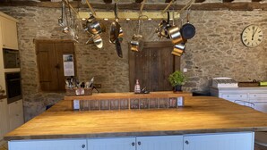 Una cocina con ollas colgantes, encimera de madera, un reloj y una pared de piedra.