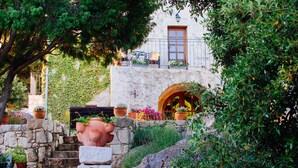 Un bâtiment en pierre avec une porte en bois et un balcon. Des plantes en pot et des fleurs sont disposées sur les marches menant à la porte.