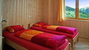 Une pièce en bois avec deux lits, chacun agrémenté de draps rouges et oranges, et une fenêtre donnant sur des collines verdoyantes.