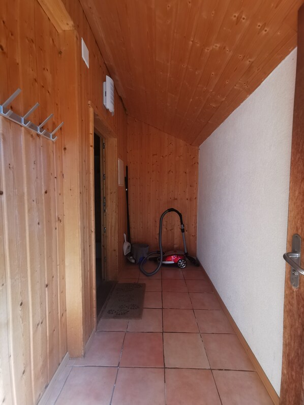 A narrow hallway with wooden walls and a tiled floor, leading to a door. A vacuum cleaner is placed against the wall.