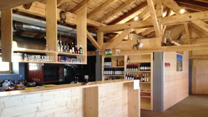 Un coin bar en bois, avec des étagères remplies de bouteilles et de verres, un réfrigérateur et un plafond en bois avec des poutres apparentes.