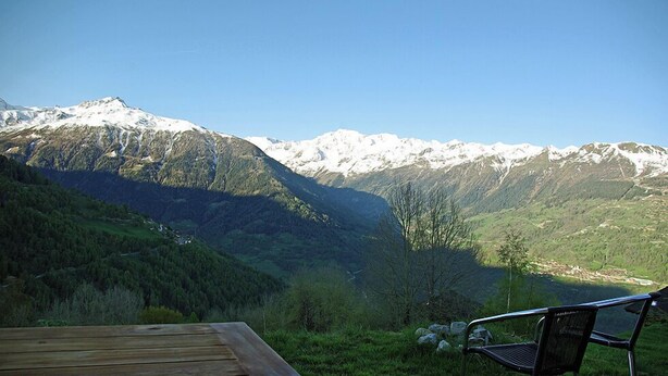 Un paysage de montagne avec une terrasse en bois et une chaise en métal.