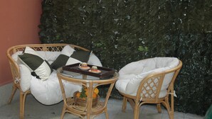 Wicker chairs with cushions, a small table with a tray, and a basket of oranges.