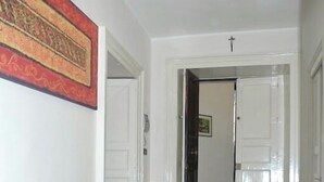 A room with a checkered rug, a wicker sofa with cushions, and a door leading to another room.