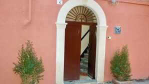 A building entrance with a brown door, a white archway, and a small blue and white tile on the wall.