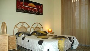 A bedroom with a bed, two nightstands, a wicker dresser, and a painting on the wall.