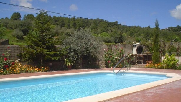 Une piscine rectangulaire avec un escalier en métal, entourée d’une terrasse carrelée de tuiles rouges.