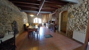 Un coin repas rustique avec un mur en pierre, des poutres en bois au plafond et un sol carrelé.