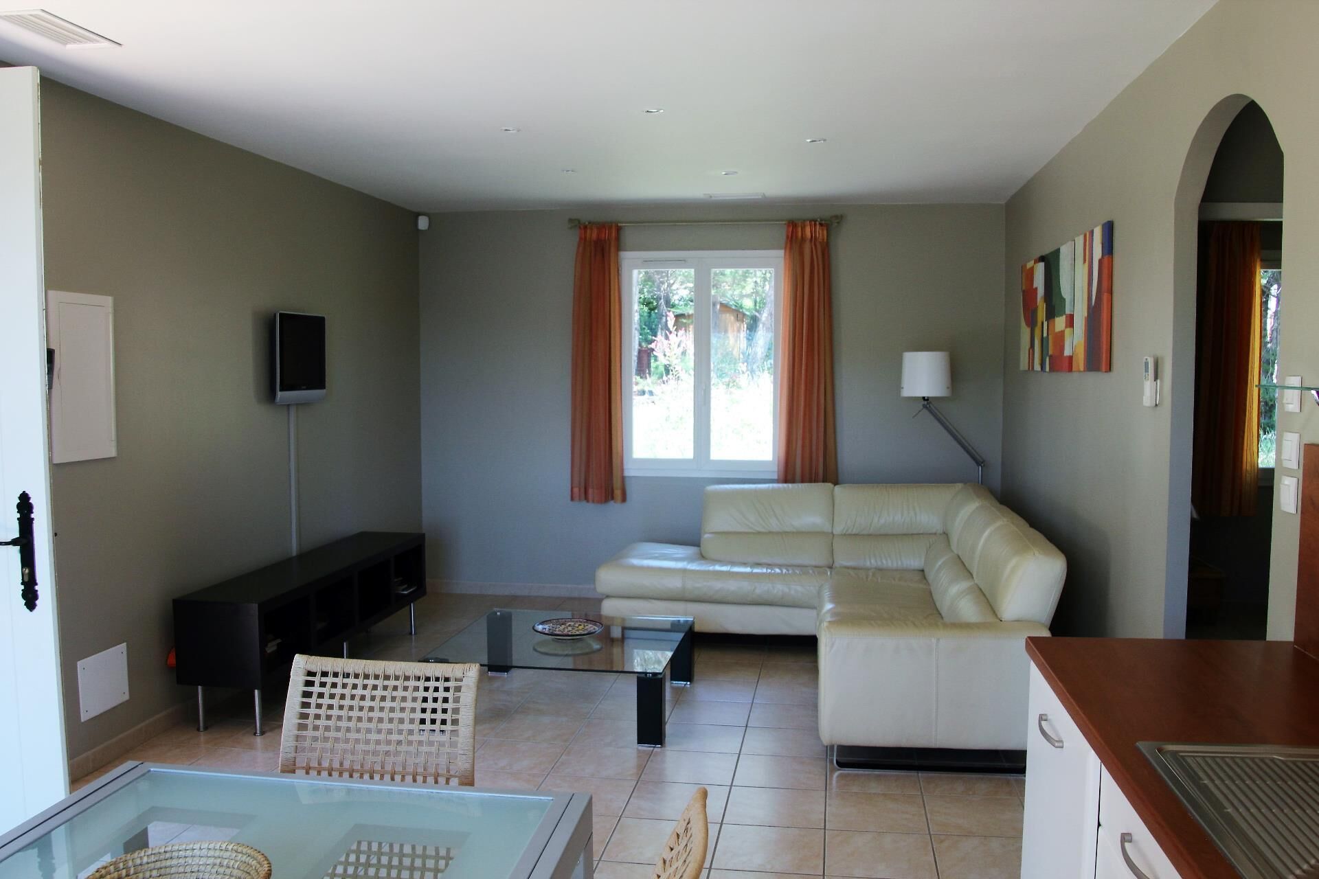 Una sala de estar con un sofá, un televisor, una mesa de centro de vidrio y una silla de mimbre.