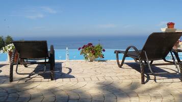 Two wicker lounge chairs facing a pool with a view of the sea.