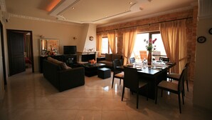 A spacious living room with a fireplace, a dining area, and a kitchen in the background. - Special Offer for August  (Corfu)
